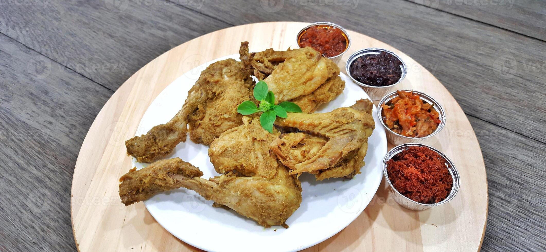 Ayam ungkep bumbu kuning or boiled chicken with curry seasoning and coconut water. Served with varian sambal or hot chili sauce. Ready to fried photo