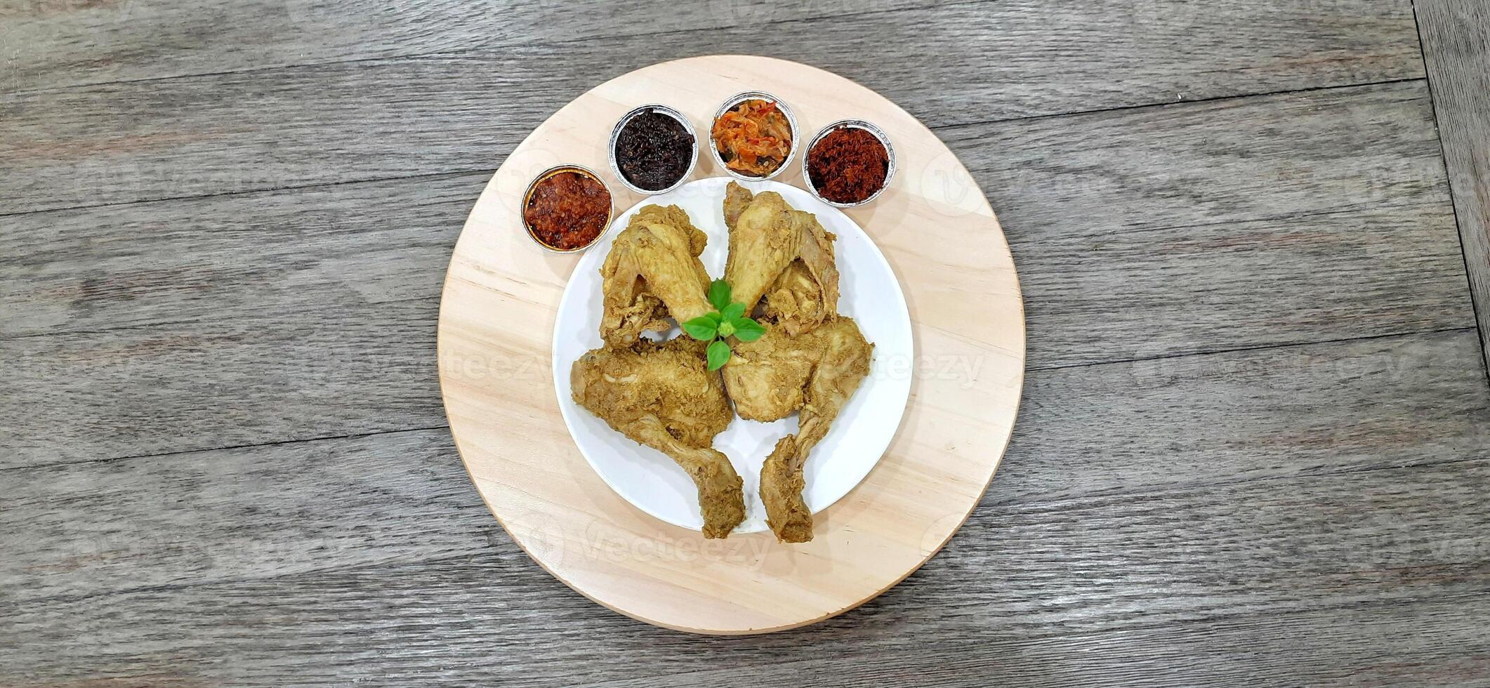 Ayam ungkep bumbu kuning or boiled chicken with curry seasoning and coconut water. Served with varian sambal or hot chili sauce. Ready to fried photo