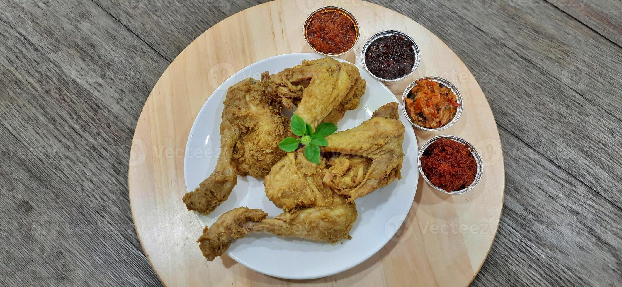 Ayam ungkep bumbu kuning or boiled chicken with curry seasoning and coconut water. Served with varian sambal or hot chili sauce. Ready to fried photo