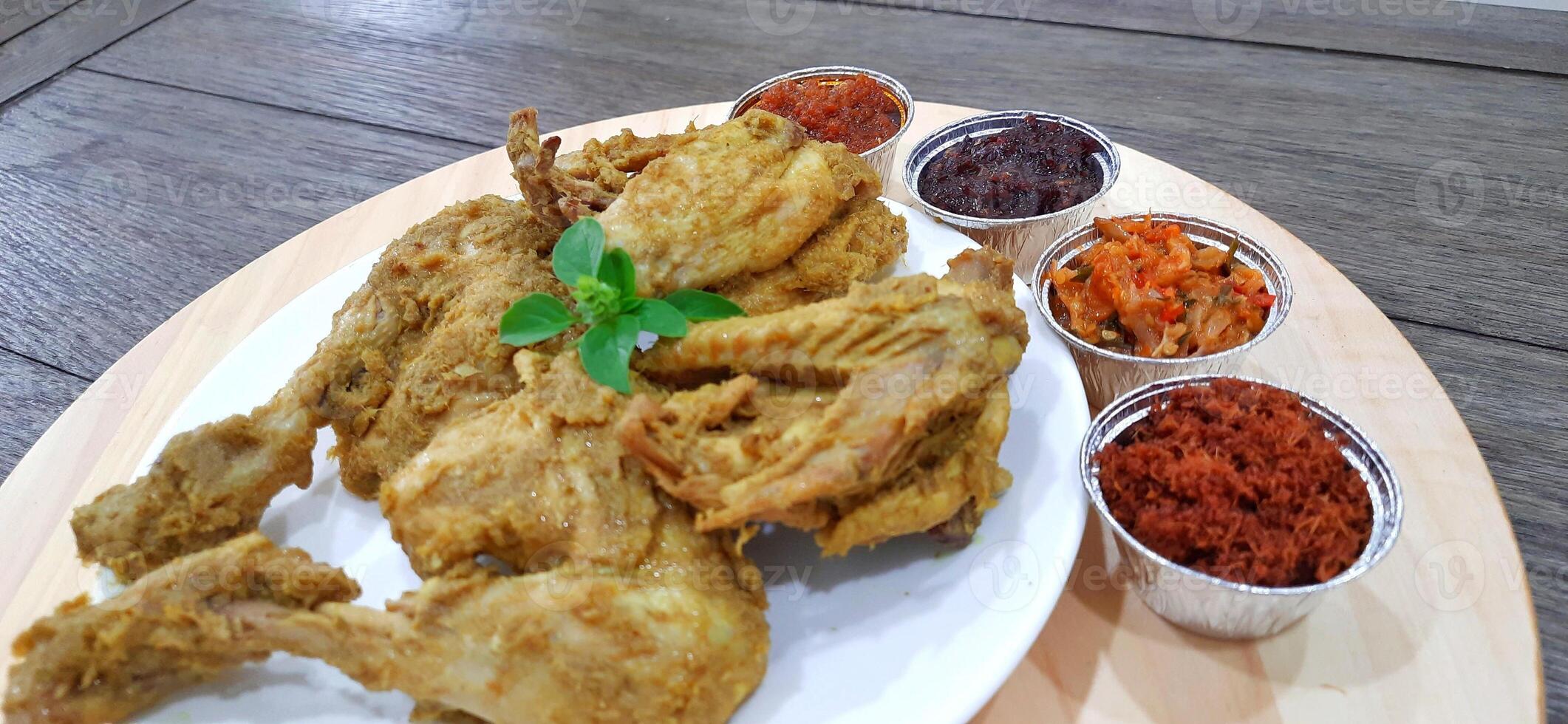 Ayam ungkep bumbu kuning or boiled chicken with curry seasoning and coconut water. Served with varian sambal or hot chili sauce. Ready to fried photo