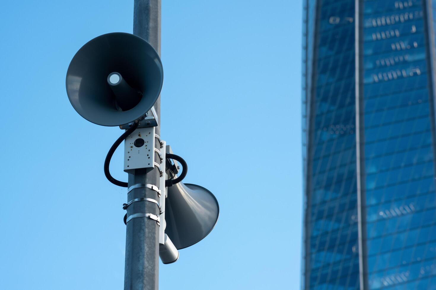 street loudspeakers on a pole against the background of a glass facade of a modern building photo