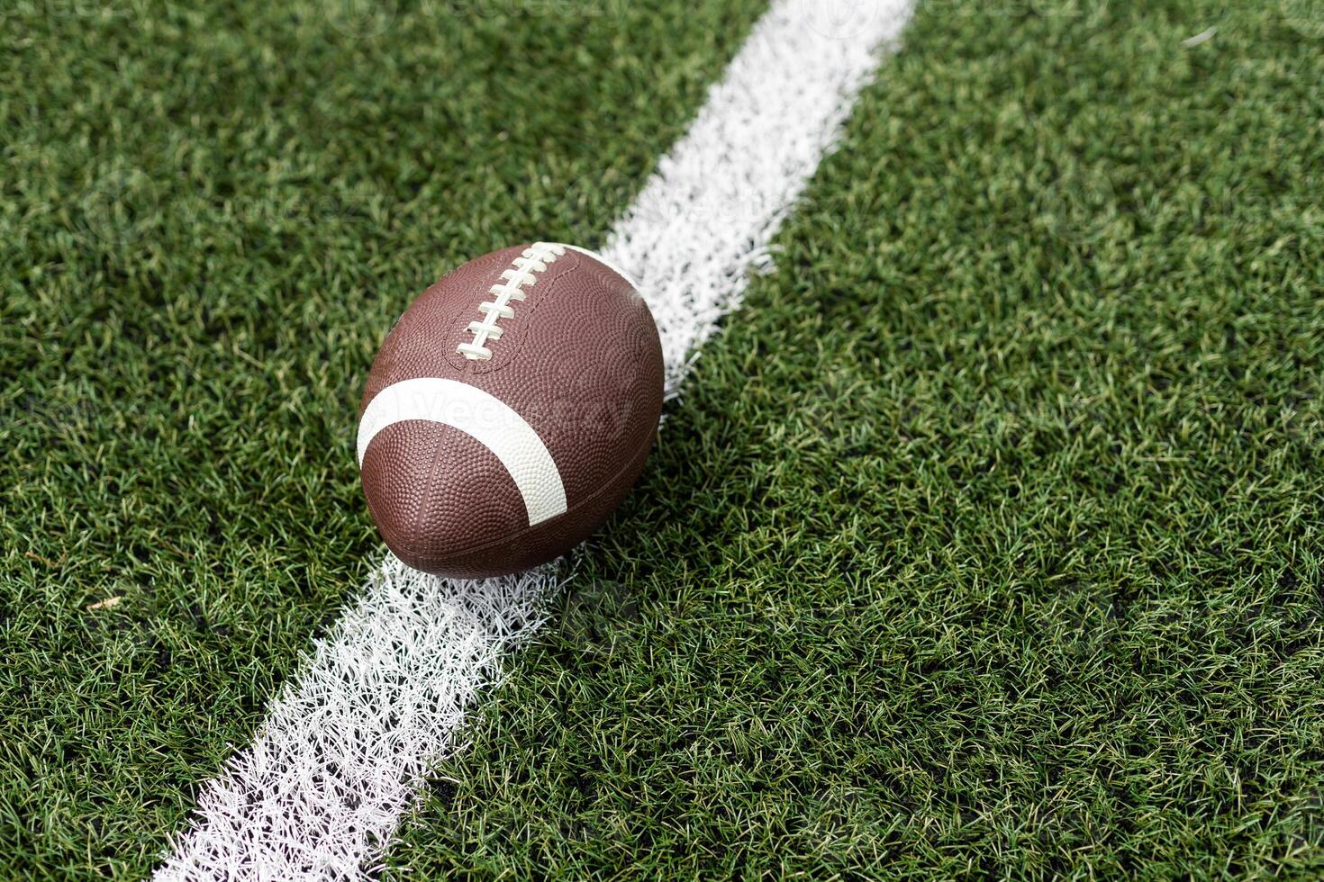 Close up view of an American Football sitting on a grass football field on the yard line. Generic Sports image photo