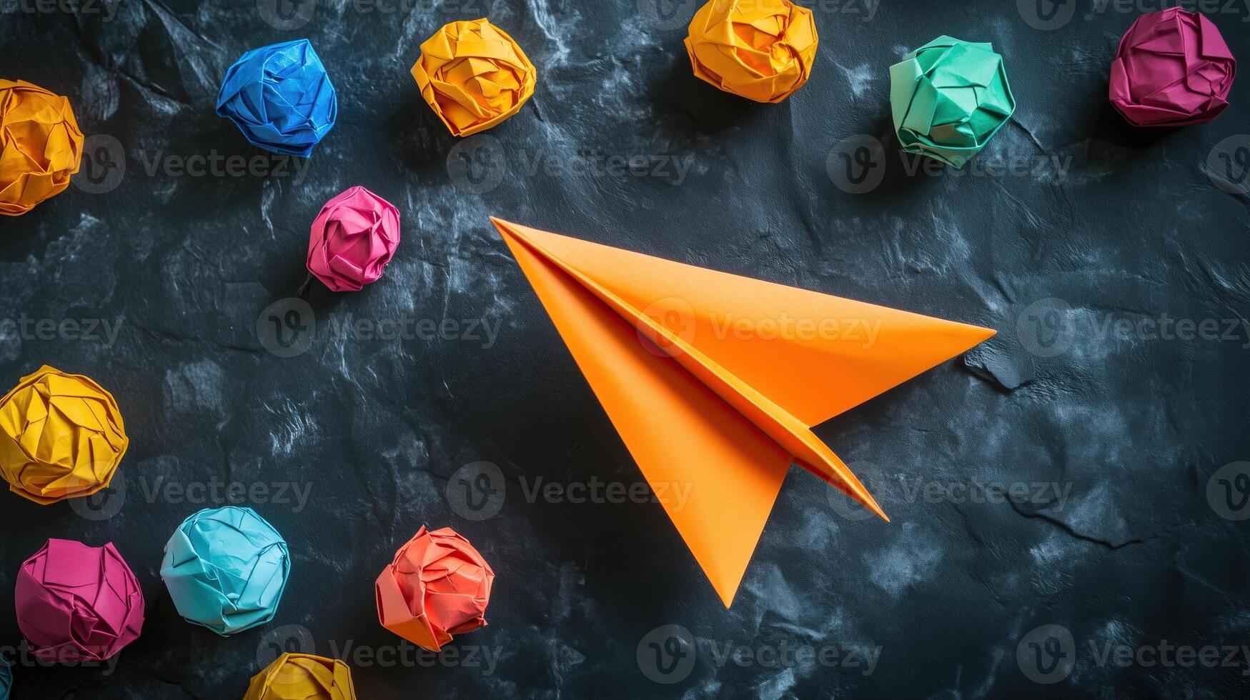 An orange paper airplane surrounded by colorful crumpled paper photo