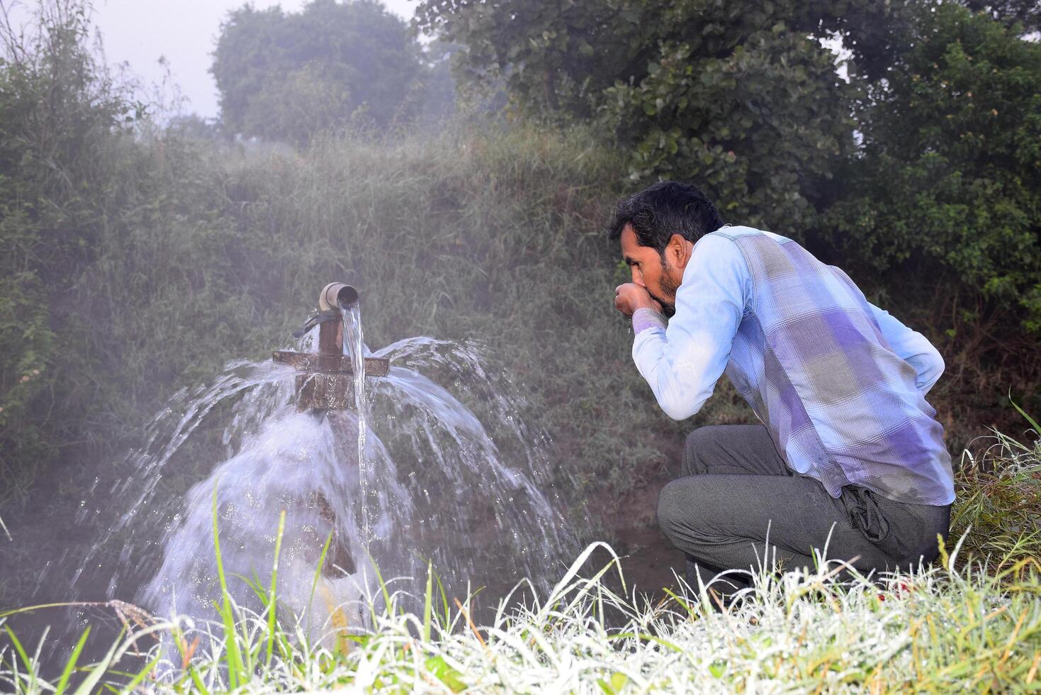 Agricultural equipment for field irrigation, an Indian farmer drinking water from water jet overflowing on his farm, Rain fog, selective focus photo