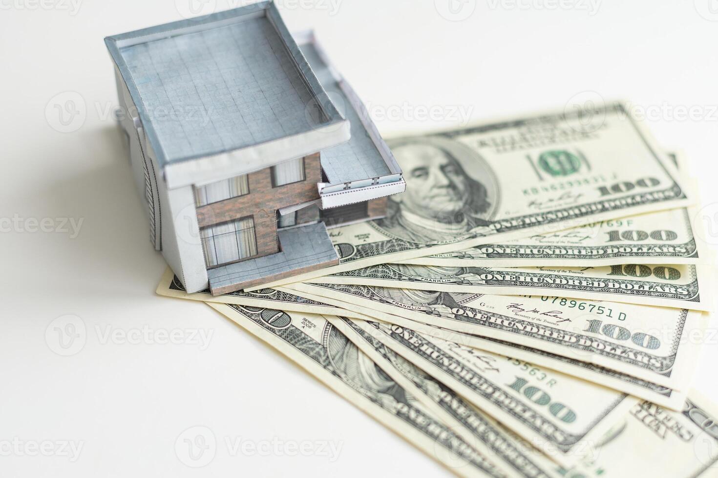A small house lies on a fan of hundred dollar bills. The keys to the purchased house. Reduced copy of the house on a white background photo