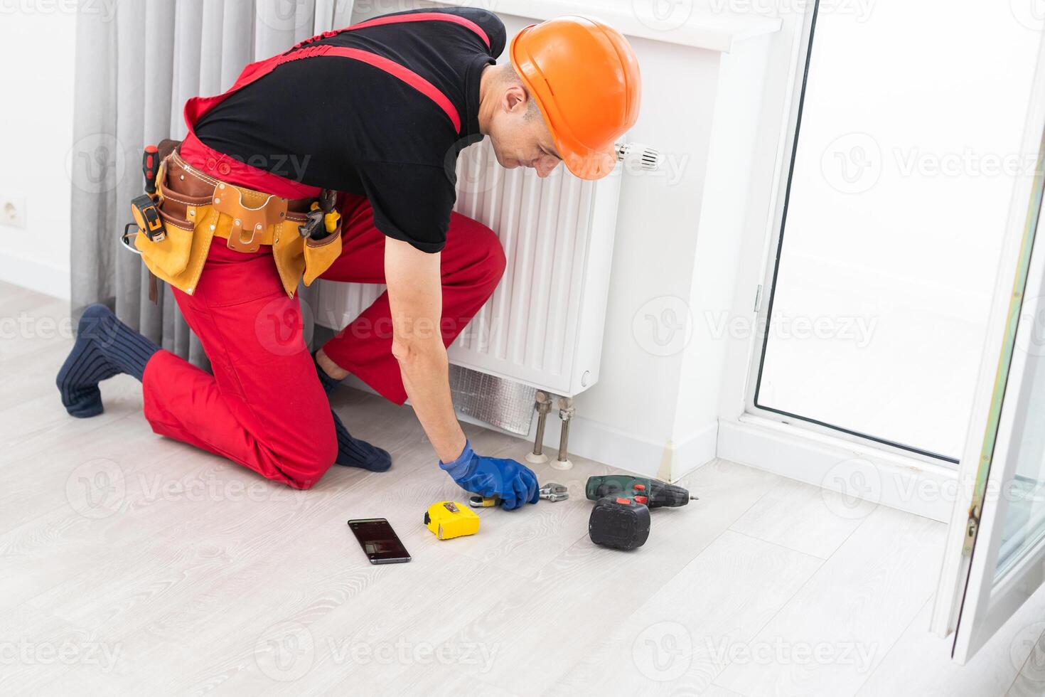 Man in work overalls using wrench while installing heating radiator in room. Young plumber installing heating system in apartment. Concept of radiator installation, plumbing works and home renovation photo
