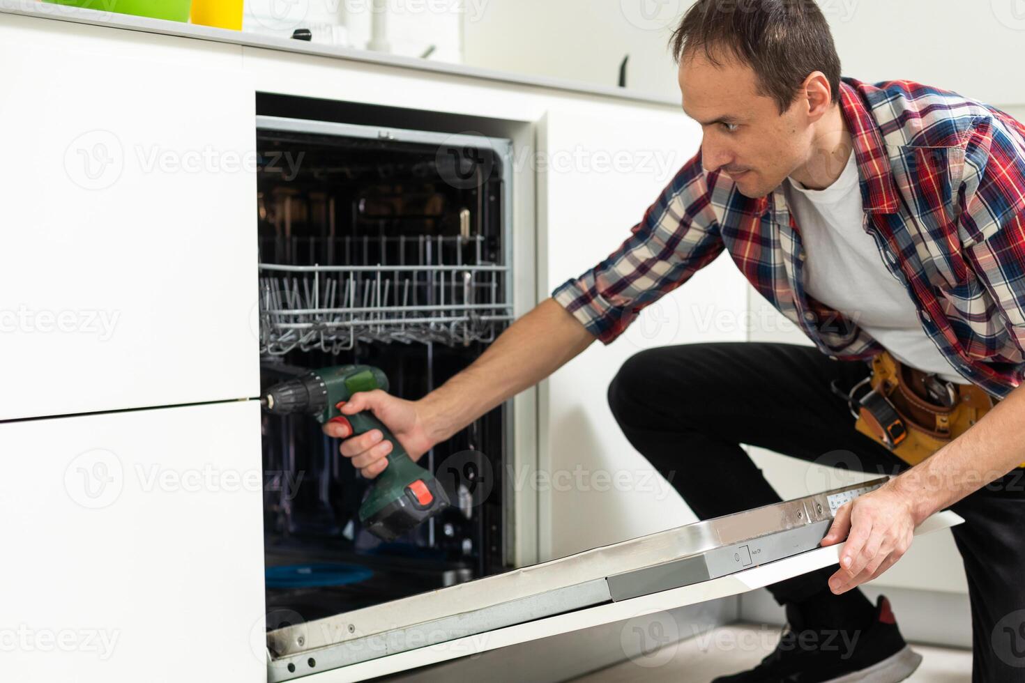 Young Male Technician Repairing Dishwasher In Kitchen photo