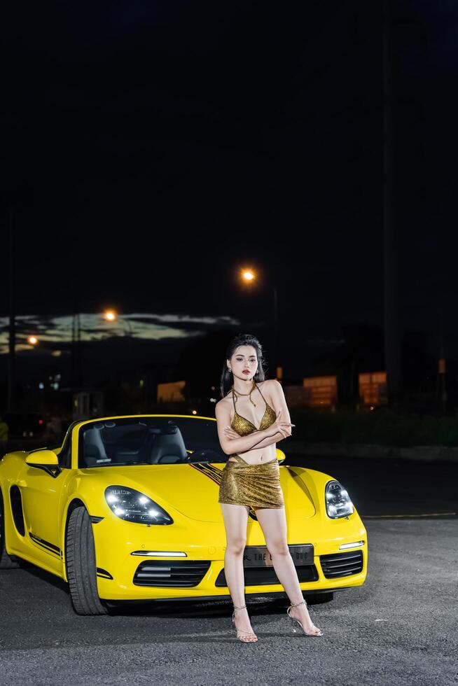 Hanoi, Vietnam - 26 Jun 2024 Beautiful young woman wearing bikini with Porsche 718 Boxster parked on the street during fashion photoshoot. photo