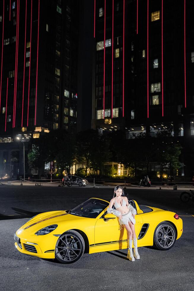 Hanoi, Vietnam - 26 Jun 2024 Beautiful young woman wearing bikini with Porsche 718 Boxster parked on the street during fashion photoshoot. photo