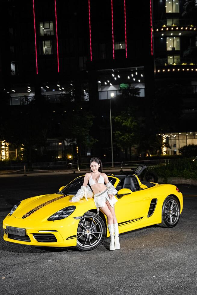 Hanoi, Vietnam - 26 Jun 2024 Beautiful young woman wearing bikini with Porsche 718 Boxster parked on the street during fashion photoshoot. photo