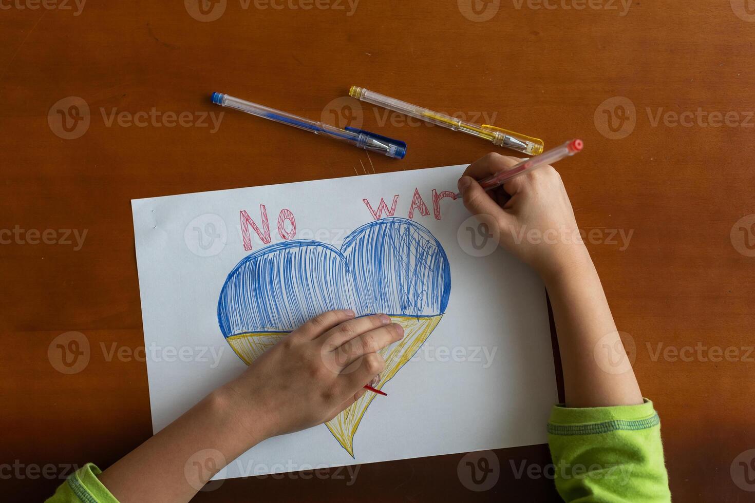 Children's hands of a child draw a heart-shaped icon with the image of the National Flag of Ukraine. View from above. Children against war. Children's drawing for peace in Ukraine photo