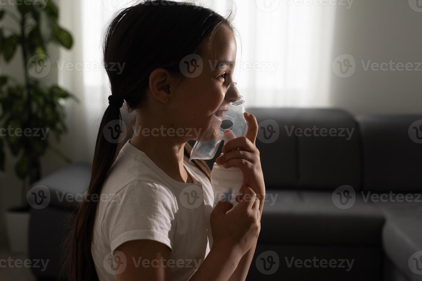 Nine years old kid with allergic asthma, inhaling her medication through spacer while looking at with her tired eyes photo