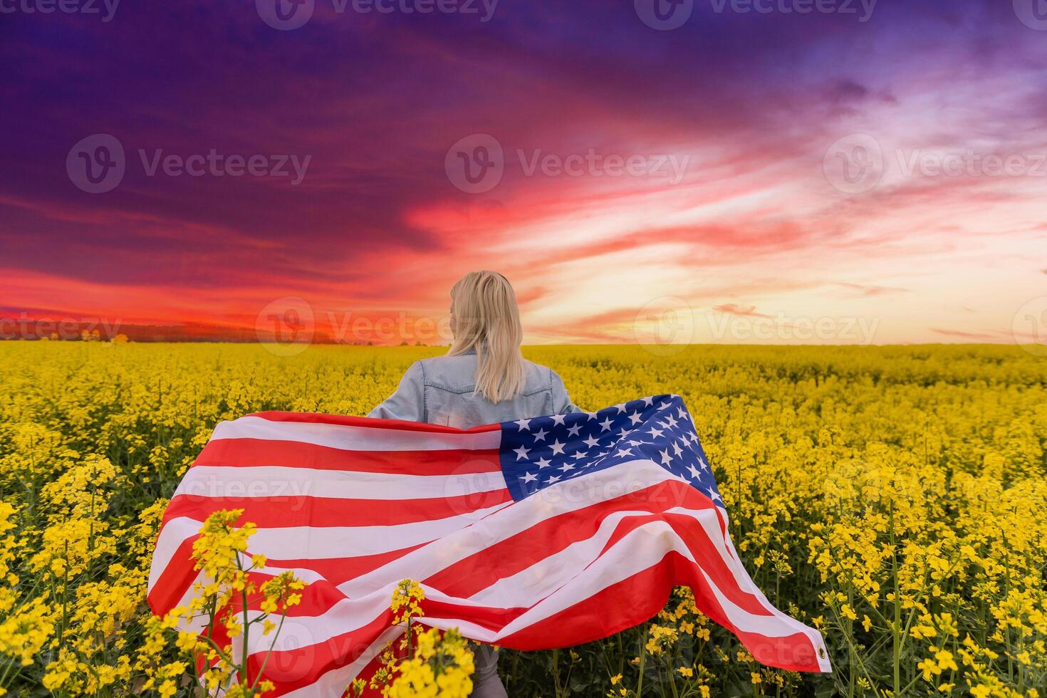 Adult woman holding American flag with pole, stars and stripe in a yellow rapeseed field. USA flag fluttering in the wind photo