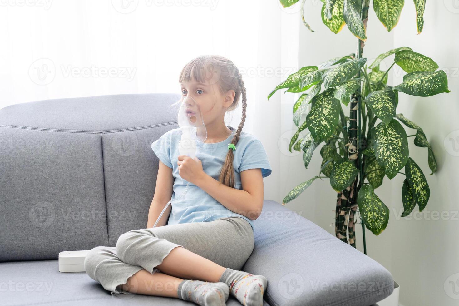Kid girl makes inhalation with a nebulizer. sick child holding inhalator in hand and breathes through an inhaler at home photo