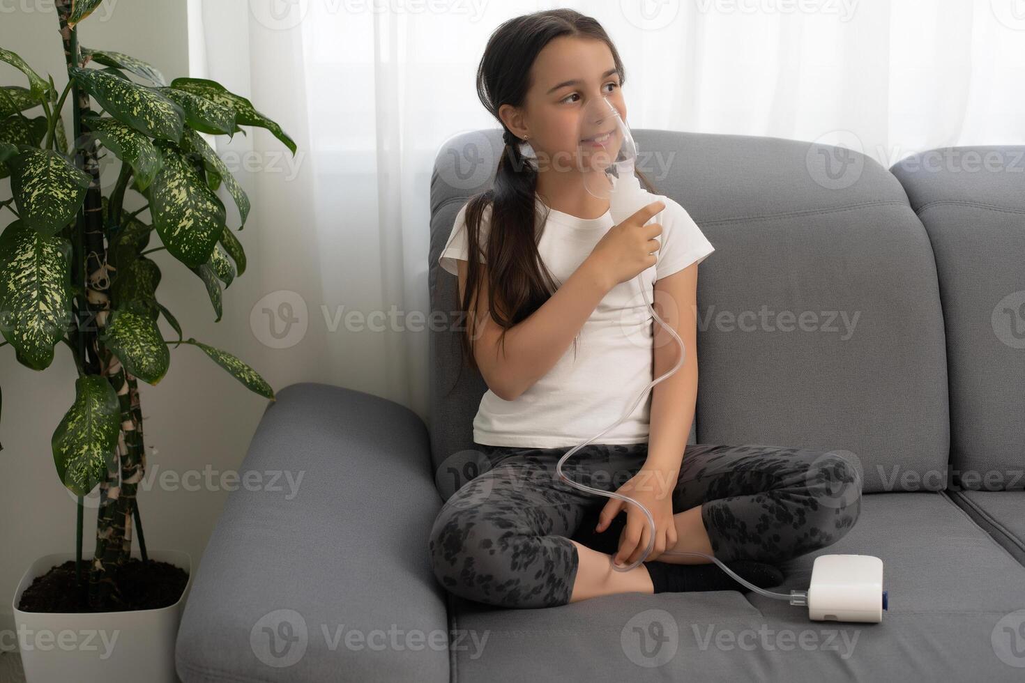 Kid girl makes inhalation with a nebulizer. sick child holding inhalator in hand and breathes through an inhaler at home photo