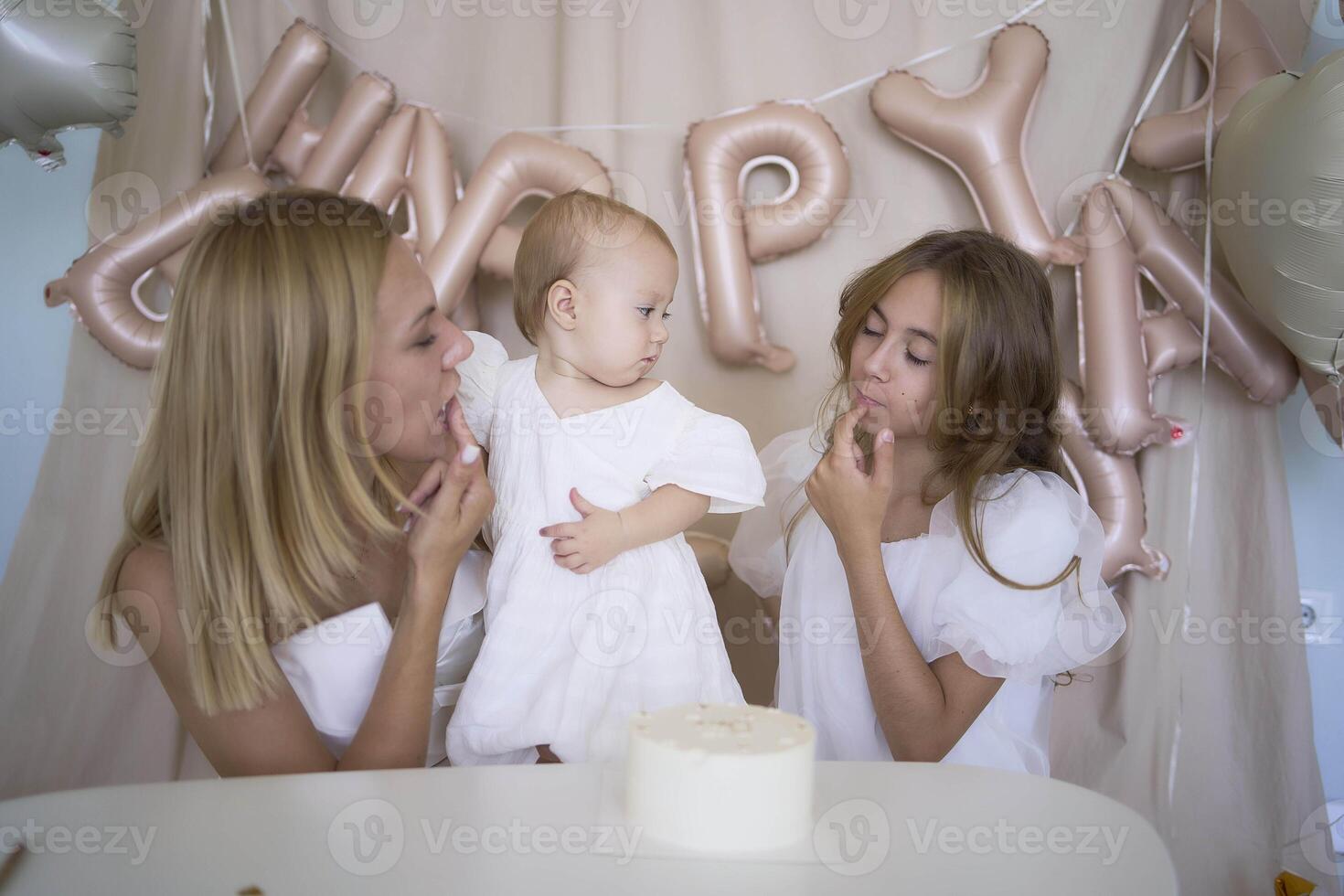baby girl tries her first birthday cake with mom and pre-teen sister photo