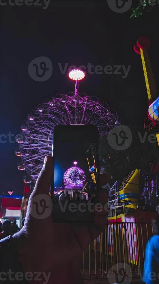 A person taking a photo of a ferris wheel at night