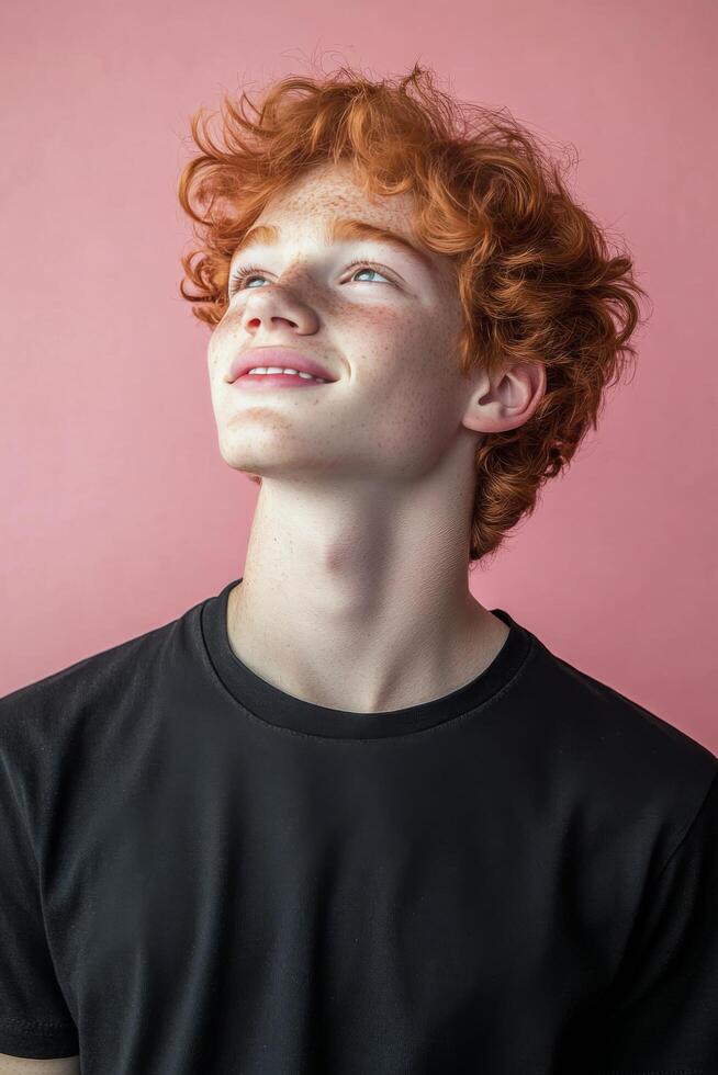 Young man with curly red hair looking up against a pink background photo