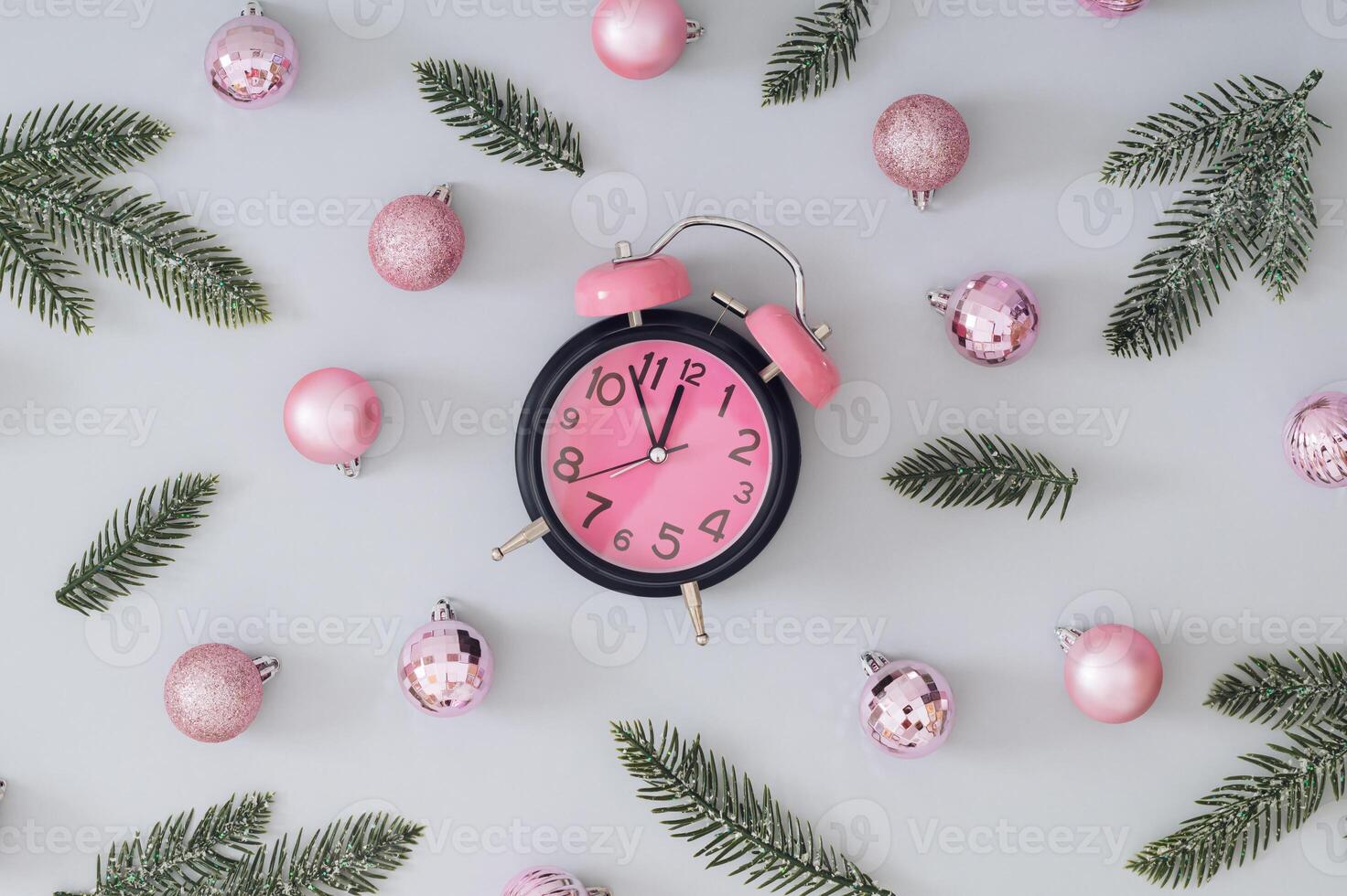 Creative trendy Christmas pattern made with pink Xmas baubles, green snowy Christmas tree branches and pink alarm clock on gray background. Minimal Christmas eve or New Year idea. Flat lay. photo