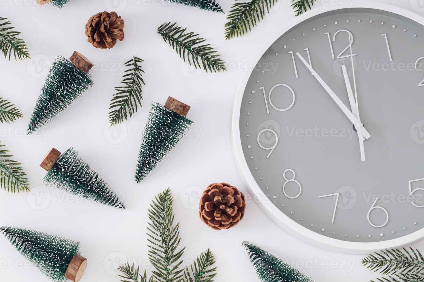 Trendy Christmas pattern made with Xmas trees, green snowy Christmas tree branches, pinecones and gray and white wall clock on gray background. Minimal Christmas eve or New Year idea. Flat lay. photo