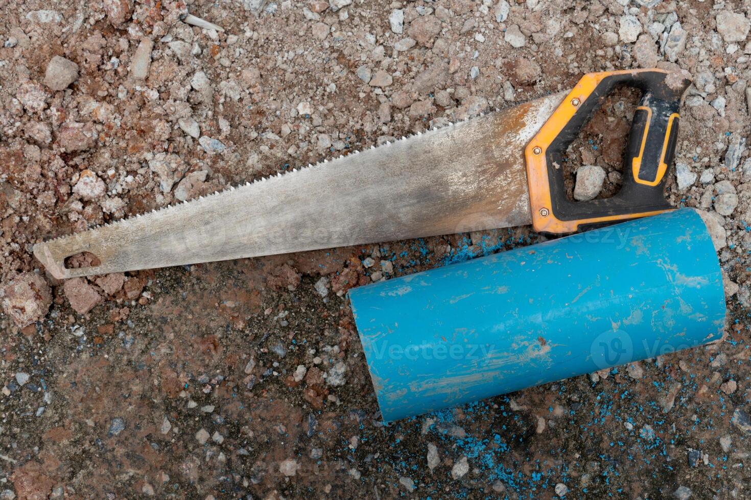 Above view of single-handed multi-purpose saw with handle. and a three-inch water pipe that was cut next to it. Gravel ground. photo