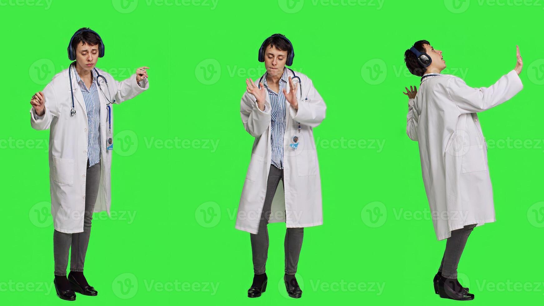 Happy woman specialist listening to cool music on headphones, having fun with modern tunes and dancing against greenscreen backdrop. Confident medic enjoys songs and shows dance moves. Camera A. photo
