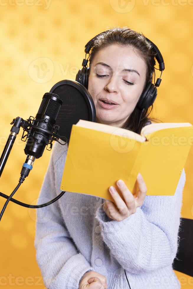 Cheerful lady narrating book word for word to produce audiobook. Joyous narrator using storytelling skills to engage audience while producing digital recording of novel, studio background photo
