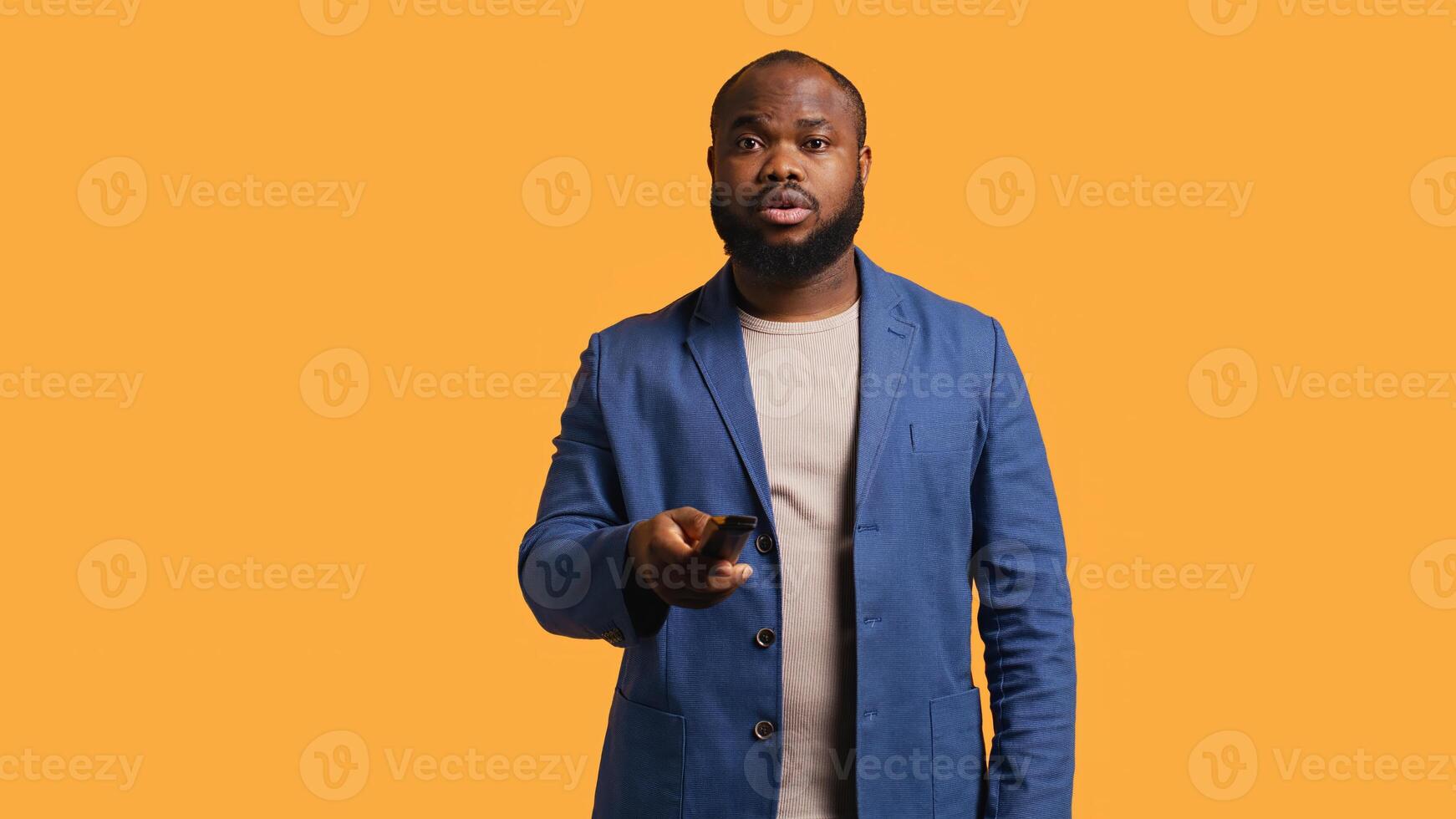 Man zapping through various TV channels, looking for entertaining content to watch, studio background. Person using remote control to select television station, switching between them, camera B photo