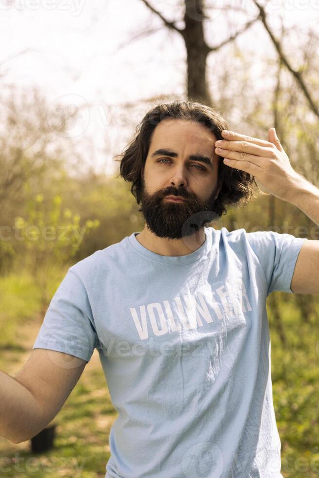 Portrait of sweaty tired male activist taking community service action, digging holes with a shovel to plant trees in the woods. Young volunteers fighting for conservation project. photo
