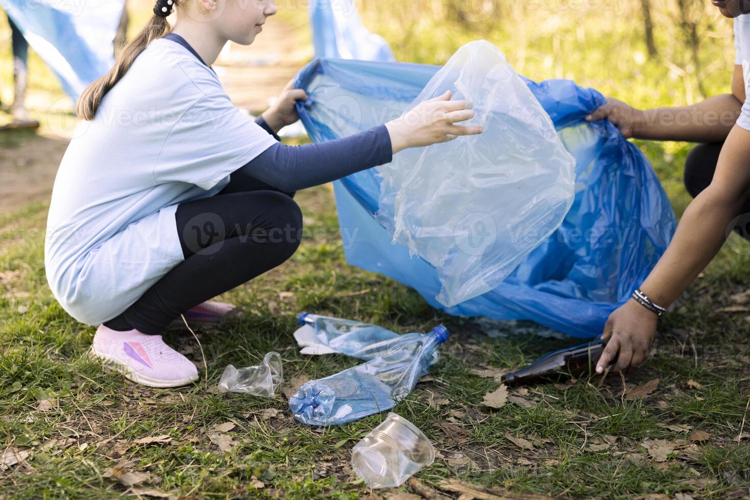 Cute small girl collecting junk in a disposal bag with her mom, recycling garbage and clearing the forest environment. Young child working with her mother to tidy up the natural ecosystem. photo