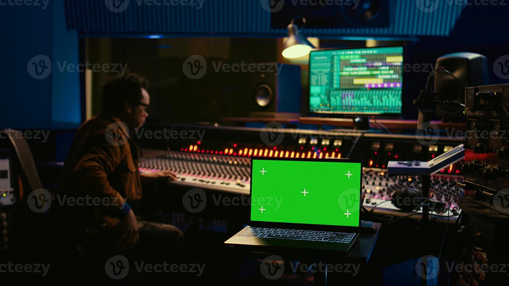 Music producer recording tracks next to laptop showing mockup isolated display, working with mixing console and mastering techniques in control room. Audio engineer producing new tunes. Camera B. photo