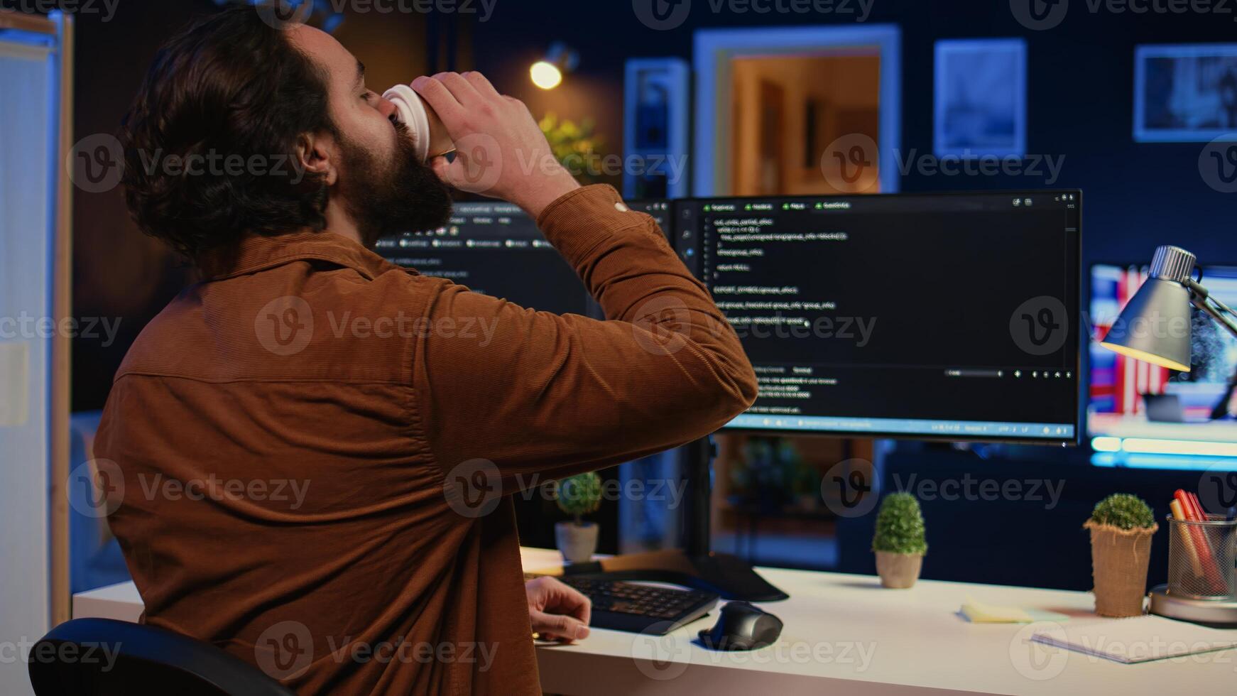 Remote software developer arriving in personal office at home, starting job shift with cup of coffee. Teleworker enjoying hot beverage while writing lines of code on computer, camera B photo