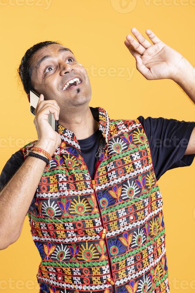 Joyous man chuckling after hearing amusing jokes from best friend over telephone call using smartphone. Person talking with humorous mate in phone call using phone, having fun, studio backdrop photo