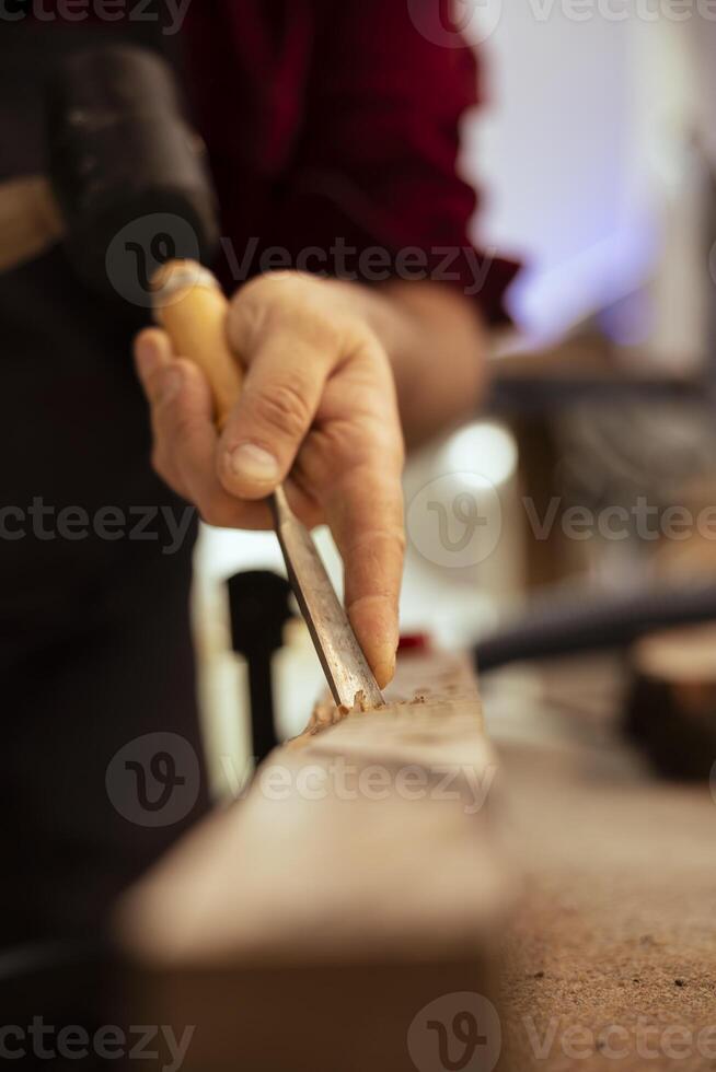Handyman carving wood using chisel and hammer in carpentry shop, enjoying diy hobby. Man using traditional crafting process to shape wooden pieces with tools, making wood art, close up shot photo