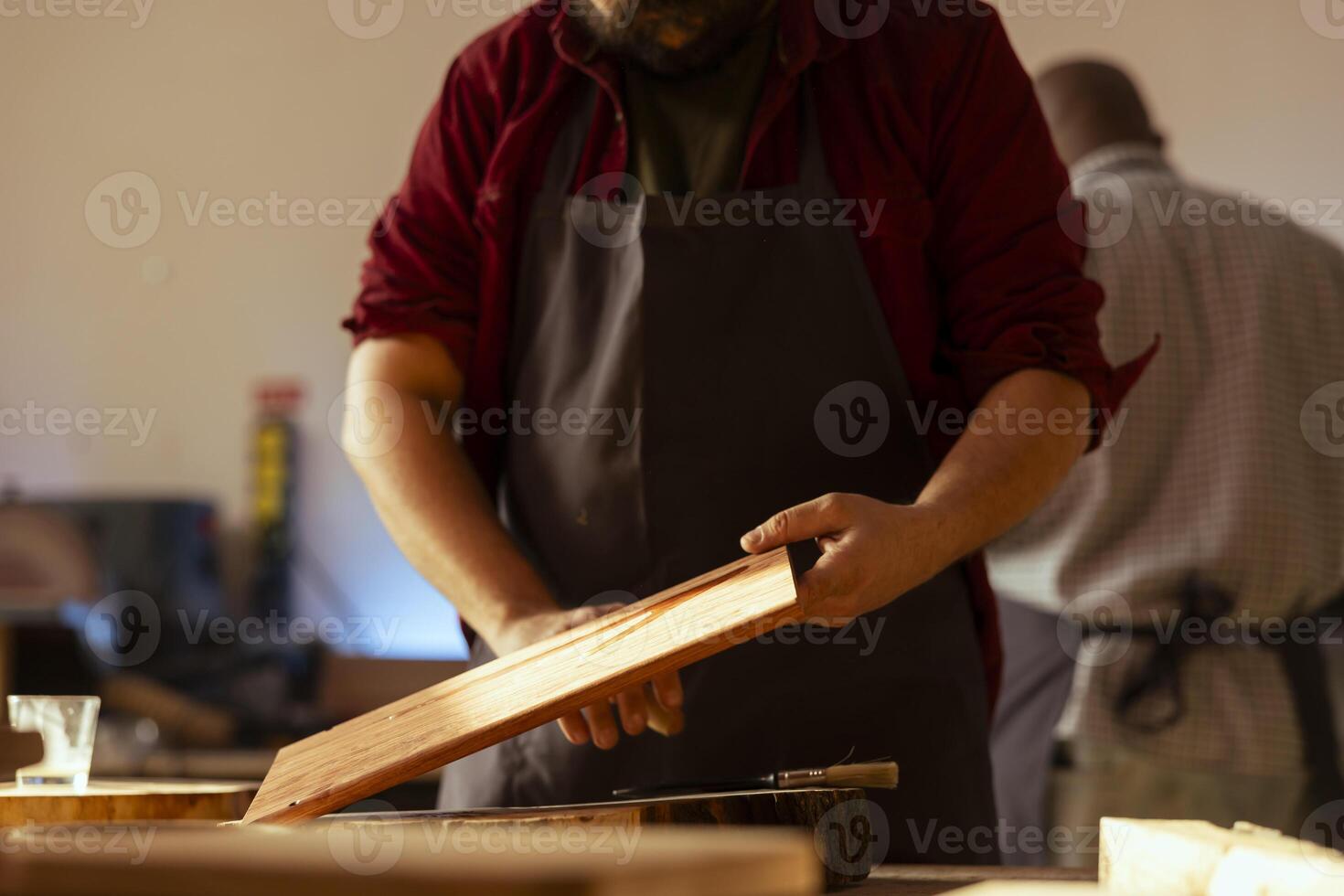 Cabinetmaker picking paintbrush to apply varnish on wooden surface, prevent damage and provide layer of protection. Manufacturer doing finishing on wood plank, putting coats of oil, enjoying diy hobby photo