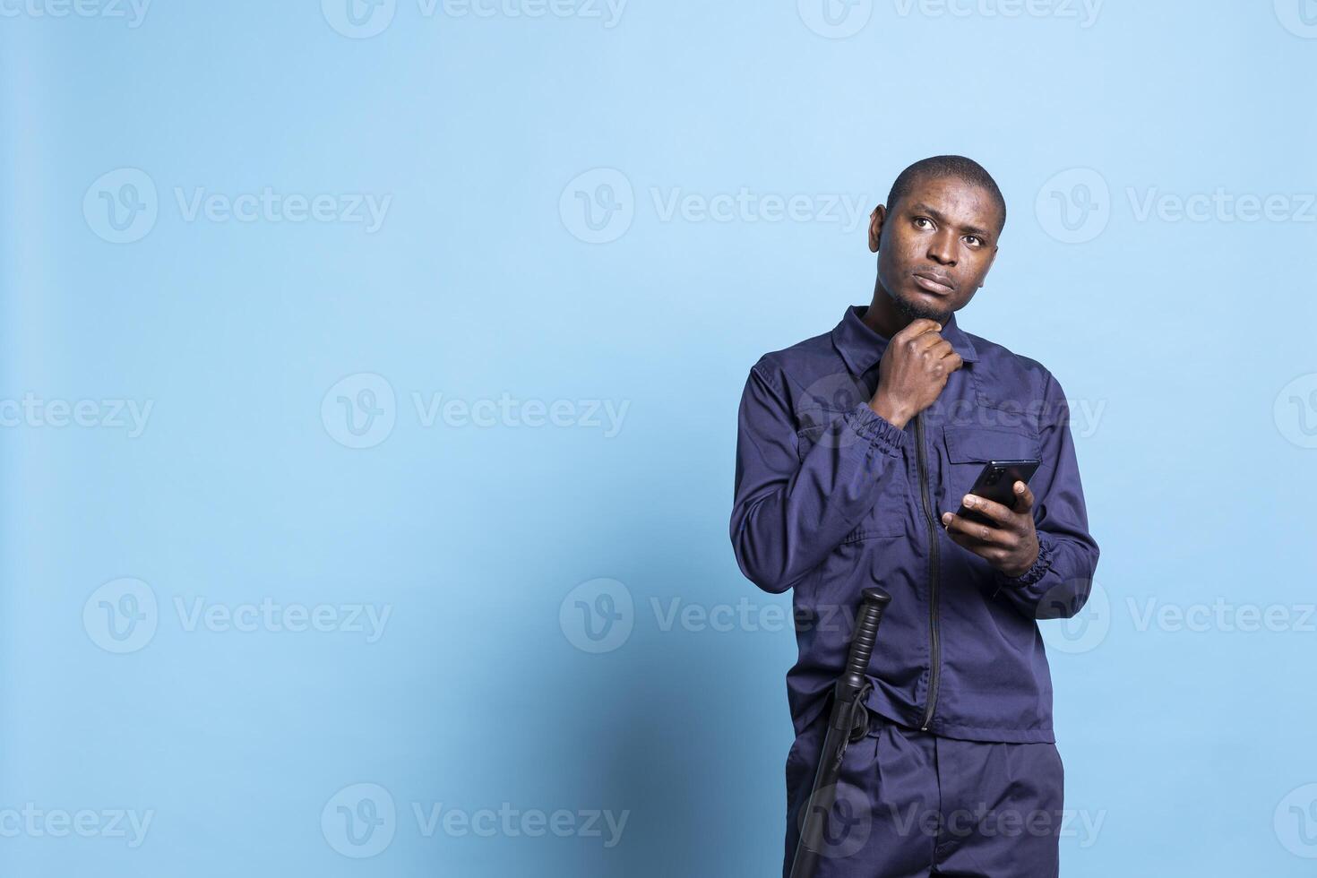 Patrol guard thinking about answers for texts on smartphone, using social media accounts to keep in touch with his friends during his job duty. Male agent checks messages online in studio. photo