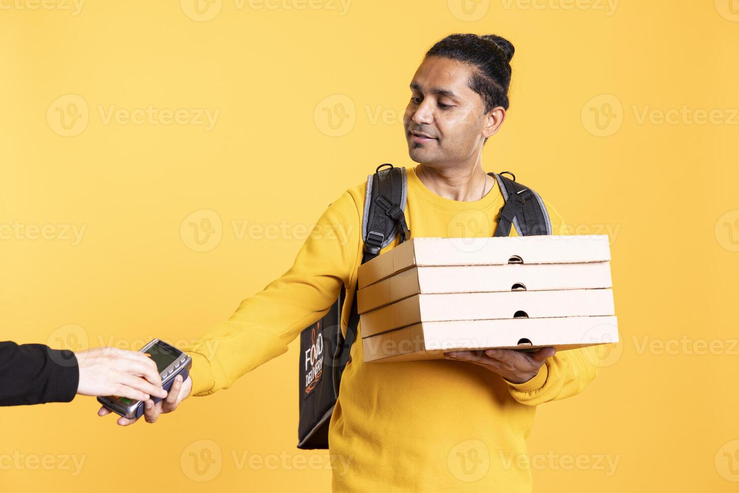 Smiling delivery worker offering takeaway order to customer paying with debit card. Client buying meal from courier, swiping card on POS device, isolated over studio background photo