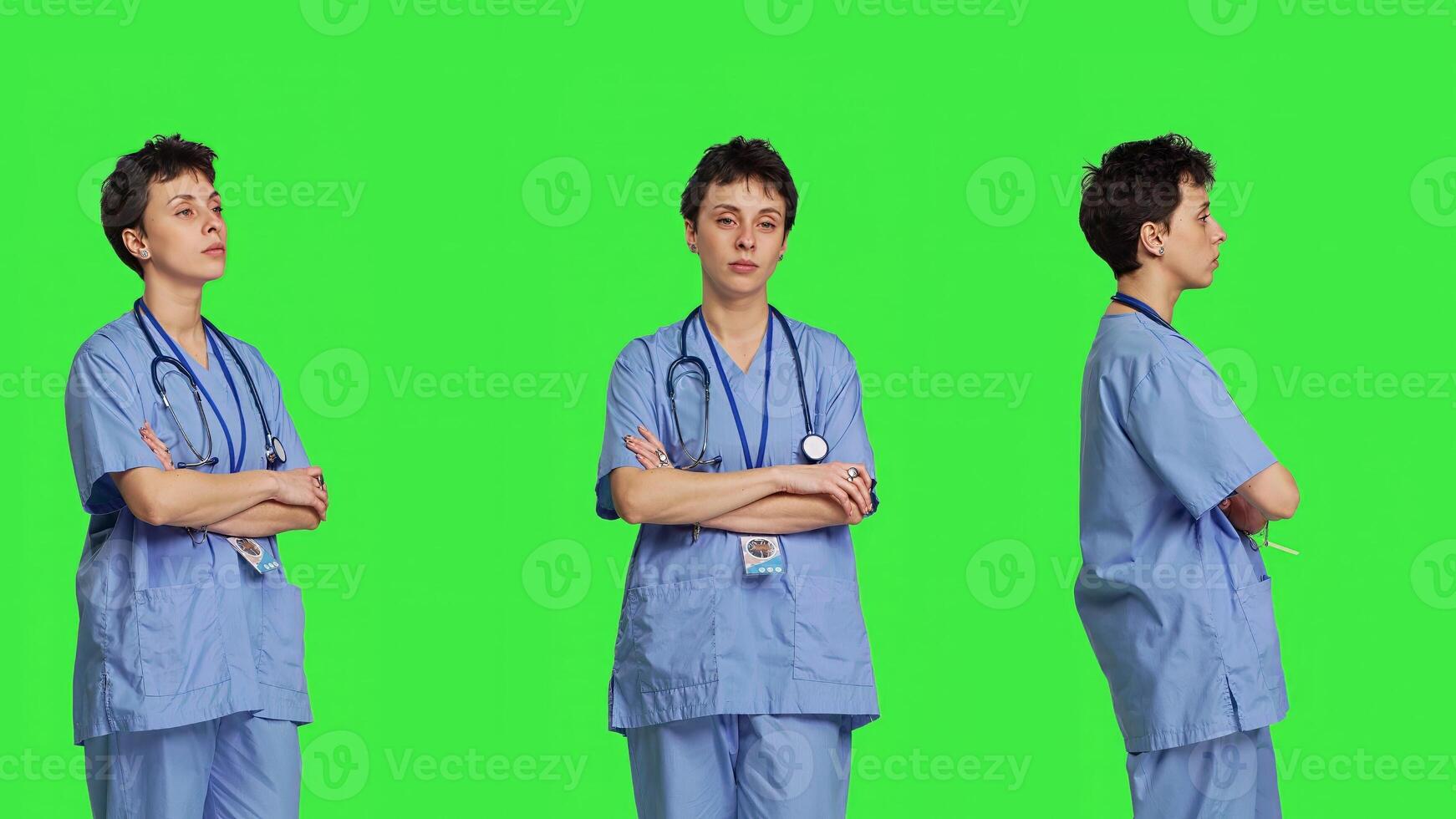 Portrait of confident medical assistant posing with arms crossed in studio, standing against greenscreen backdrop. Successful nurse with healthcare expertise wearing blue scrubs uniform. Camera B. photo
