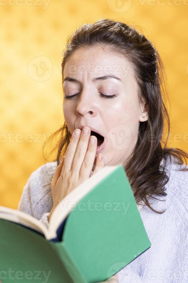 Exhausted woman yawning while reading uninteresting book needed for school exam, studio background. Tired student yearning for sleep while learning from academic textbook, close up shot photo