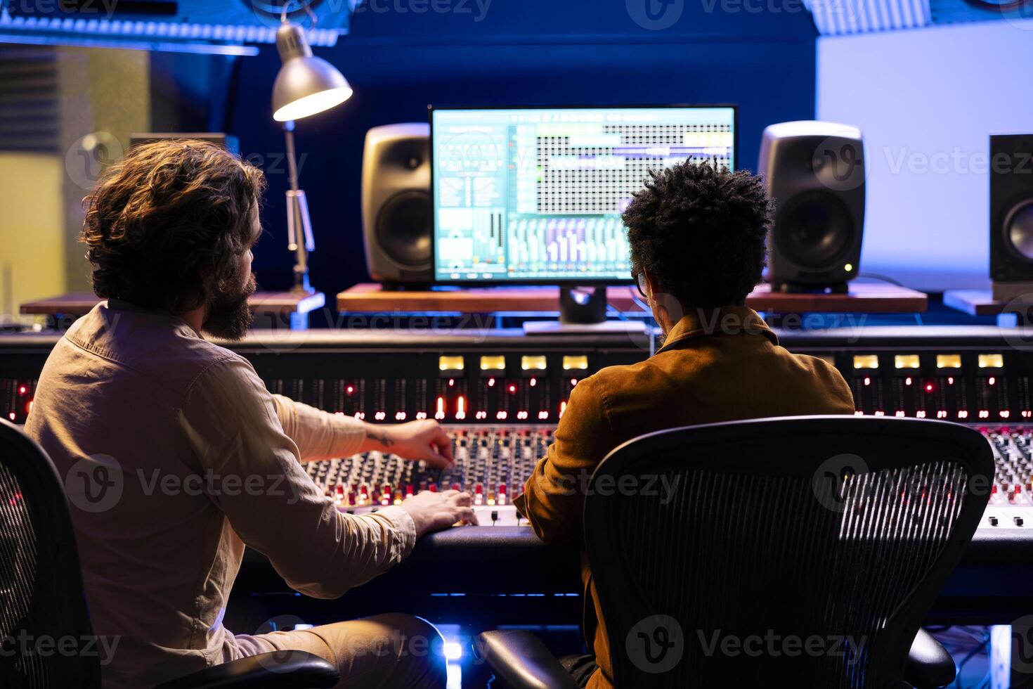 Artist and composer working together in recording music studio, collaborating on a hit song in control room. Technician mixing tunes with audio console and faders or knobs, edit records. photo