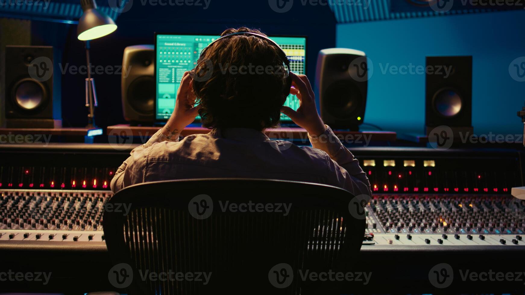 Sound designer working on track recording with audio professional software, operating technical equipment on panel board in control room. Audio engineer enhances music high quality. Camera B. photo