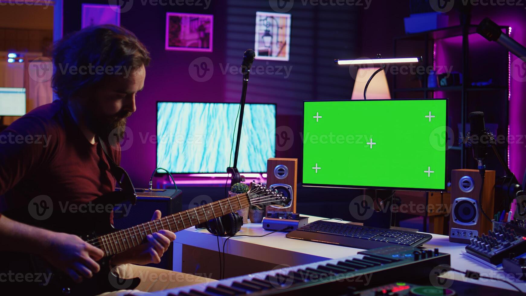 Male singer learning to play a new song on acoustic guitar, using greenscreen on computer to watch online tutorials. Artist songwriter practicing with his instrument in home studio. Camera B. photo