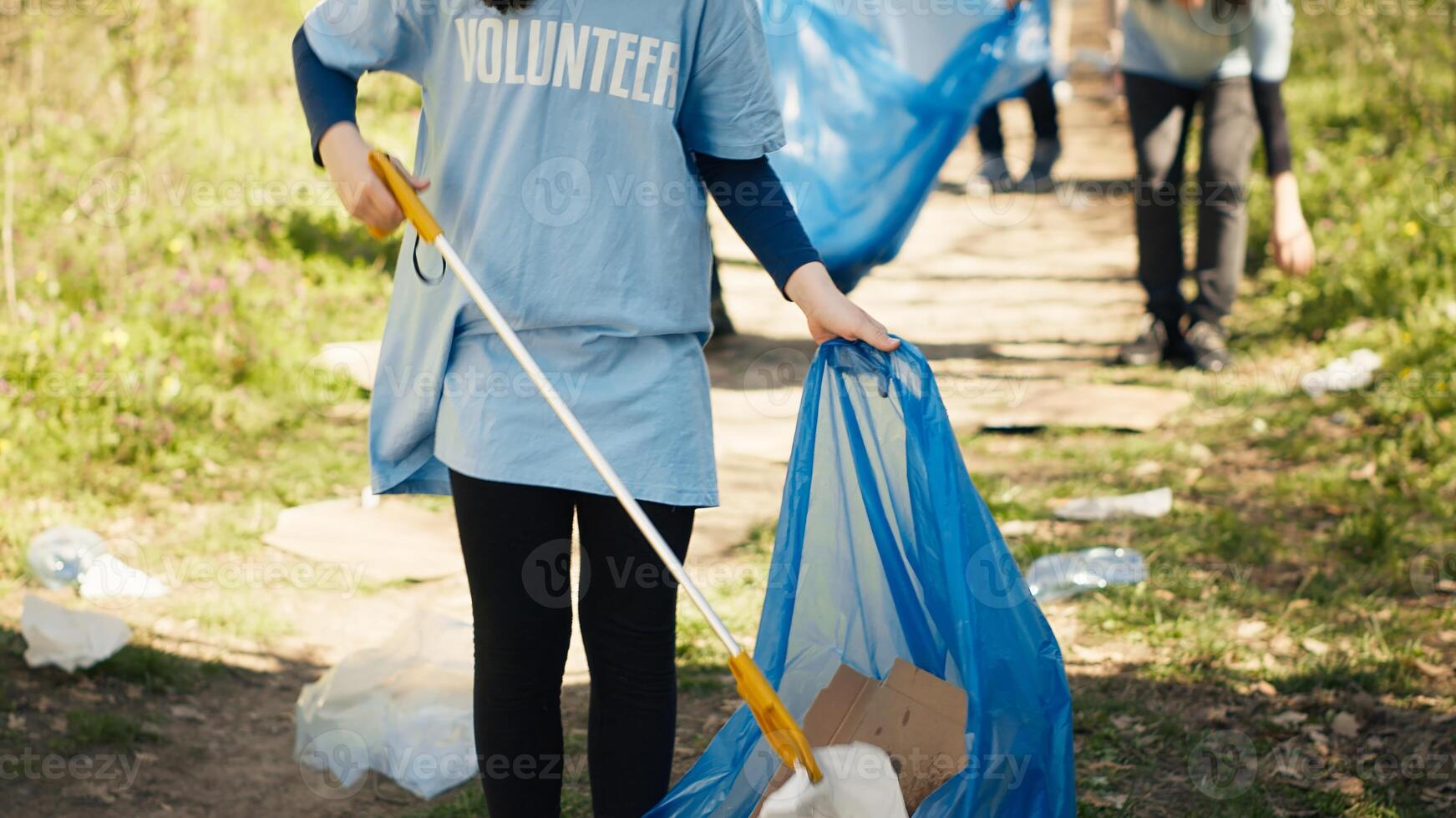 Young child using tongs tool to grab and pick up trash from the woods, collecting rubbish from a natural habitat. Little girl growing up with environmental care and recycling plastic waste. Camera A. photo