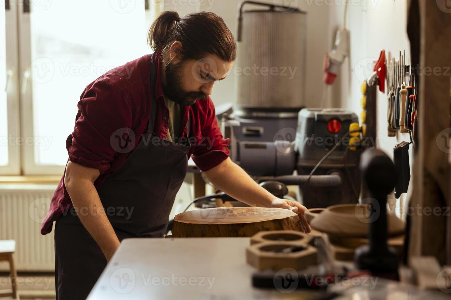 Carpenter lifting heavy wood stub, starting furniture assembling in studio. Cabinetmaker in joinery preparing to carry piece of wooden log to woodworking machine to create wooden objects photo