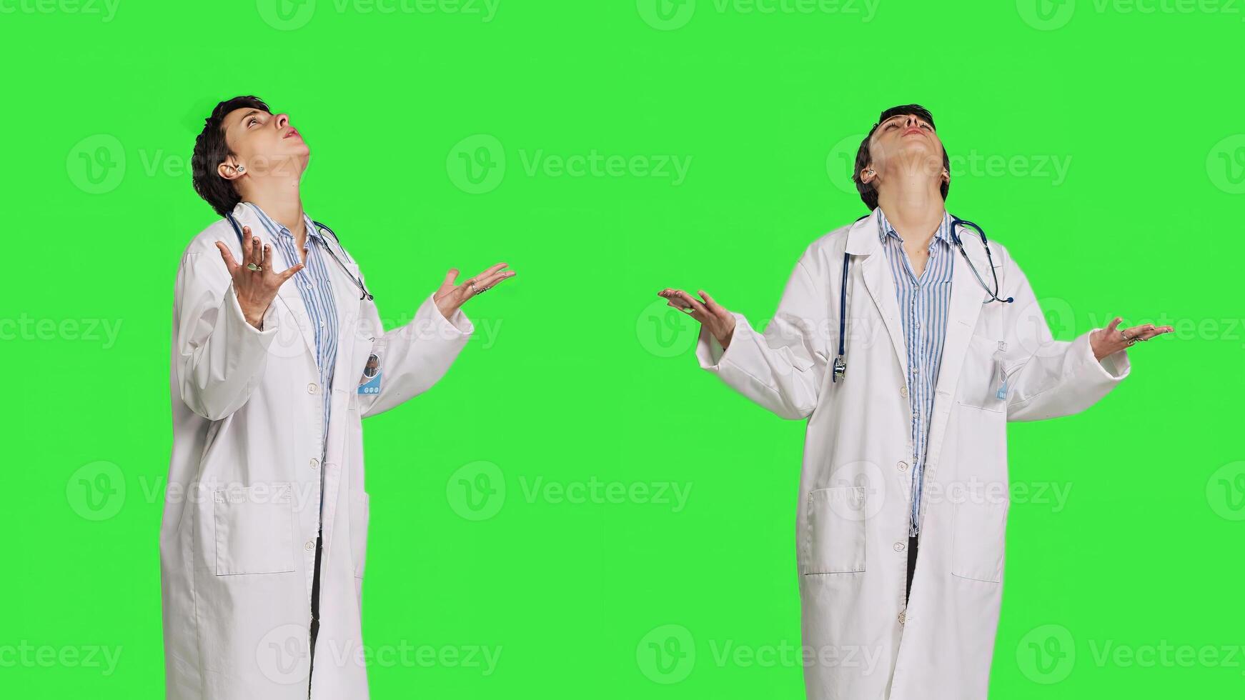 Religious woman physician praying to jesus christ against greenscreen, looking up and saying a prayer. Doctor worshipping God and meditating, spiritual medic with belief in christianity. Camera B. photo