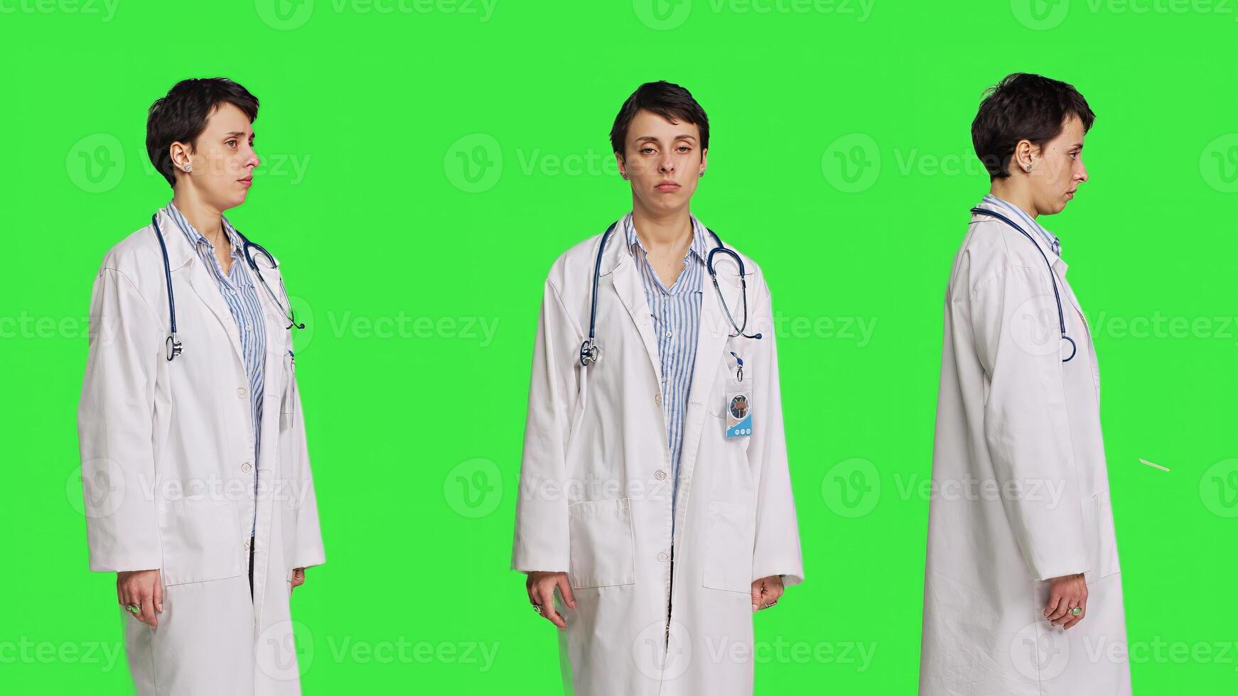 Physician saying no and showing negative reaction symbol in studio, wearing a white coat and standing against greenscreen backdrop. Woman medic feeling displeased, rejection sign. Camera B. photo
