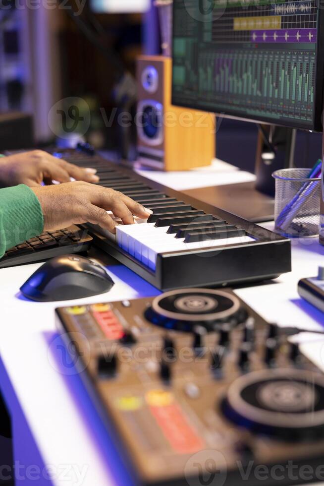 Sound designer recording his electronic piano notes in home studio, plays midi controller song and adds effects on recordings before launching music. Artist uses synthesizer and amplifier. Close up. photo