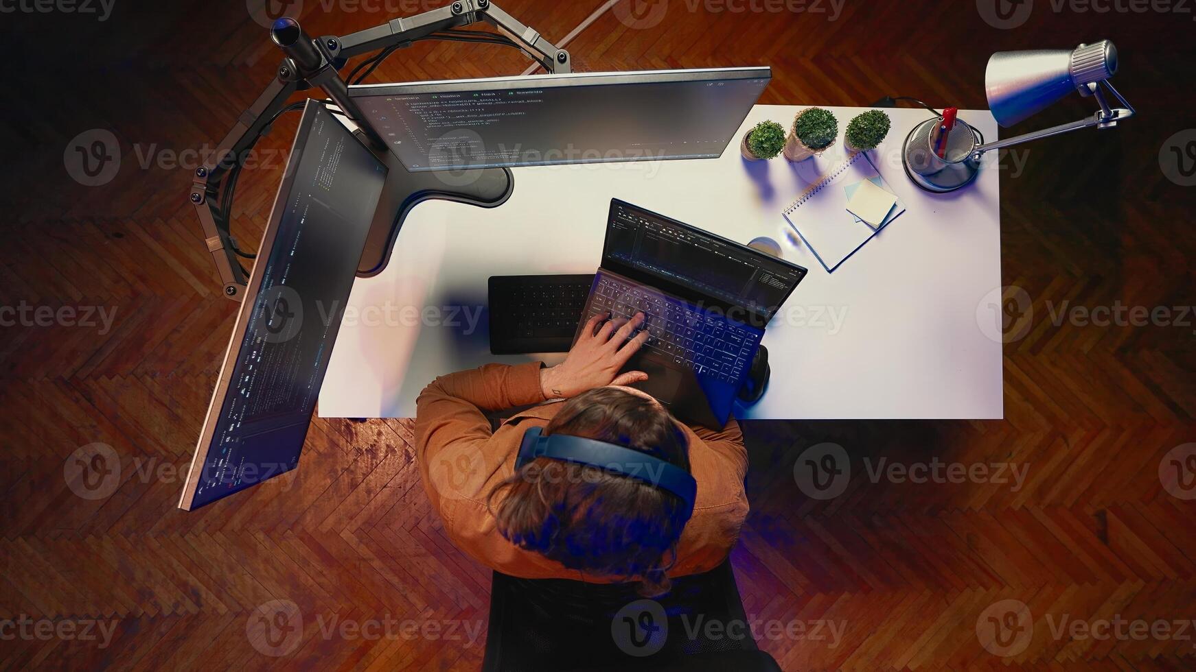 Top down view of engineer typing code in home office, using Java programming language to develop software application. It specialist using multimonitor PC setup and laptop to finish tasks, aerial shot photo