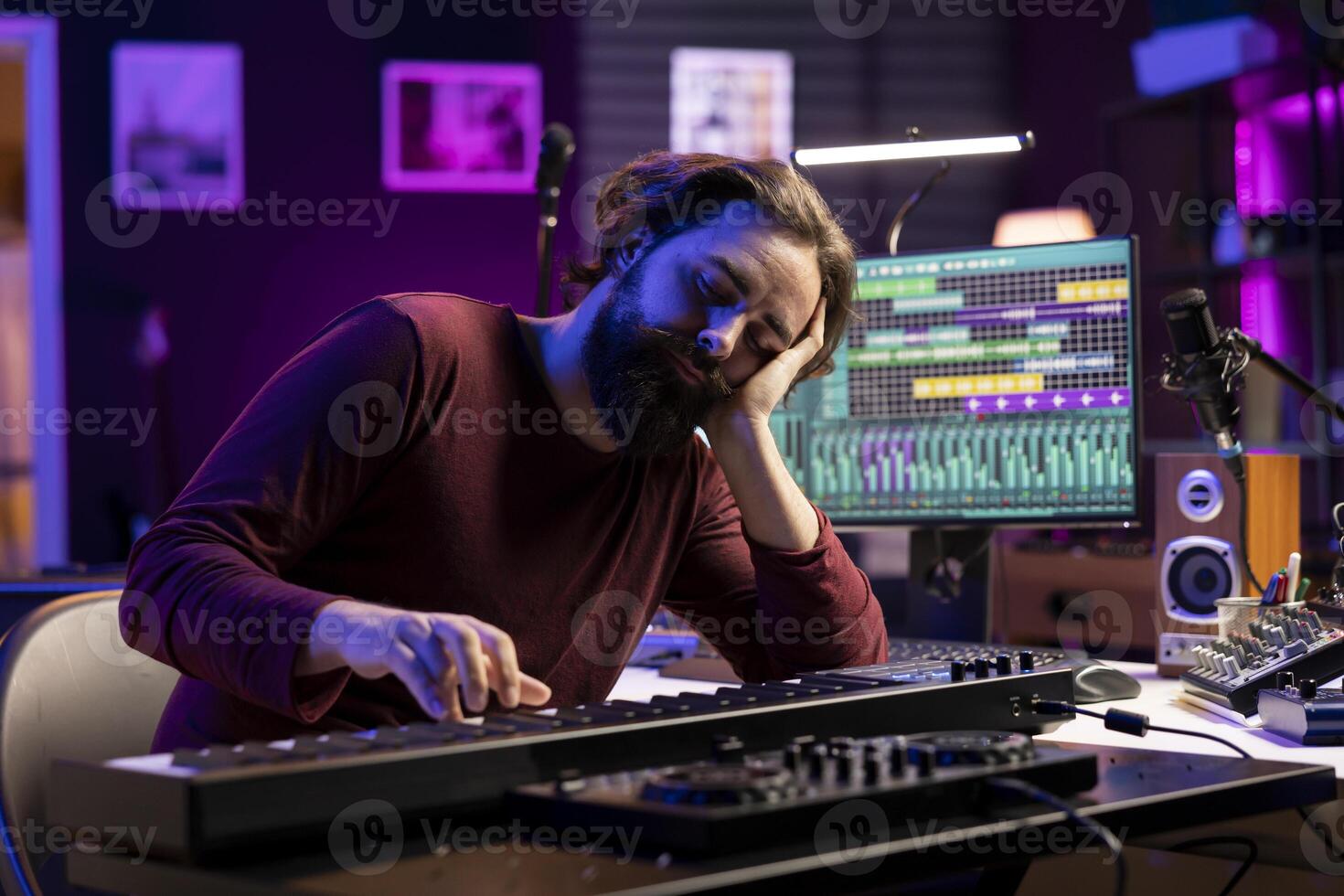 Tired artist losing sleep to learn new piano notes in home studio, playing midi controller electronic keyboard to compose songs. Producer being exhausted and stresses while he works on music. photo