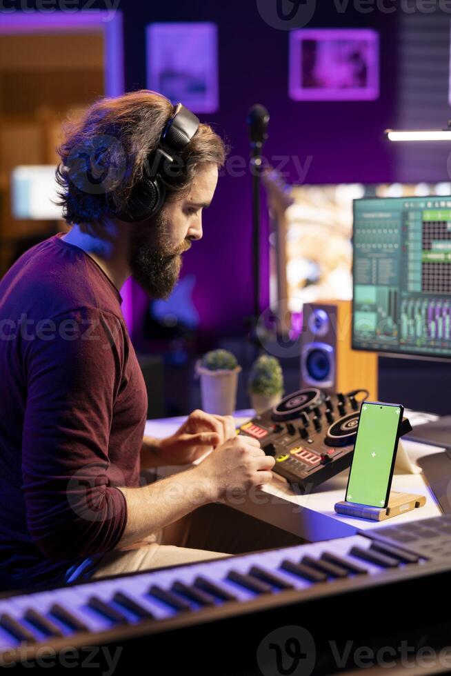 Audio engineer adding sound effects on tunes in post production, working with daw software next to greenscreen layout on mobile phone. Music producer creating sounds on mixing console. photo